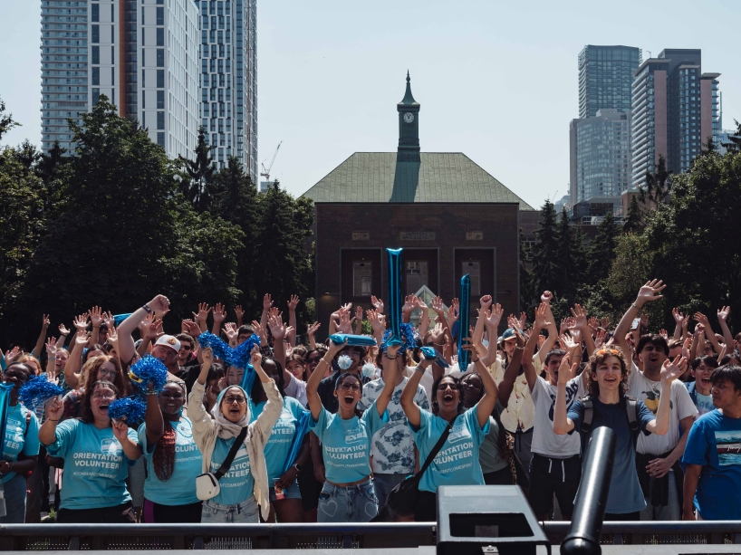 University students stand in a crowd waving their arms in the air in celebration.