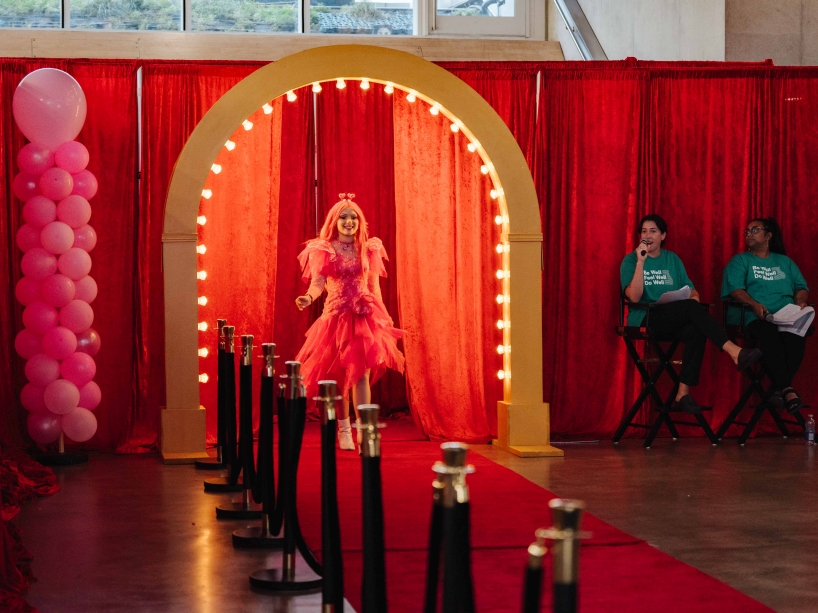 A student wearing a pink dress walks on a red carpet runway.