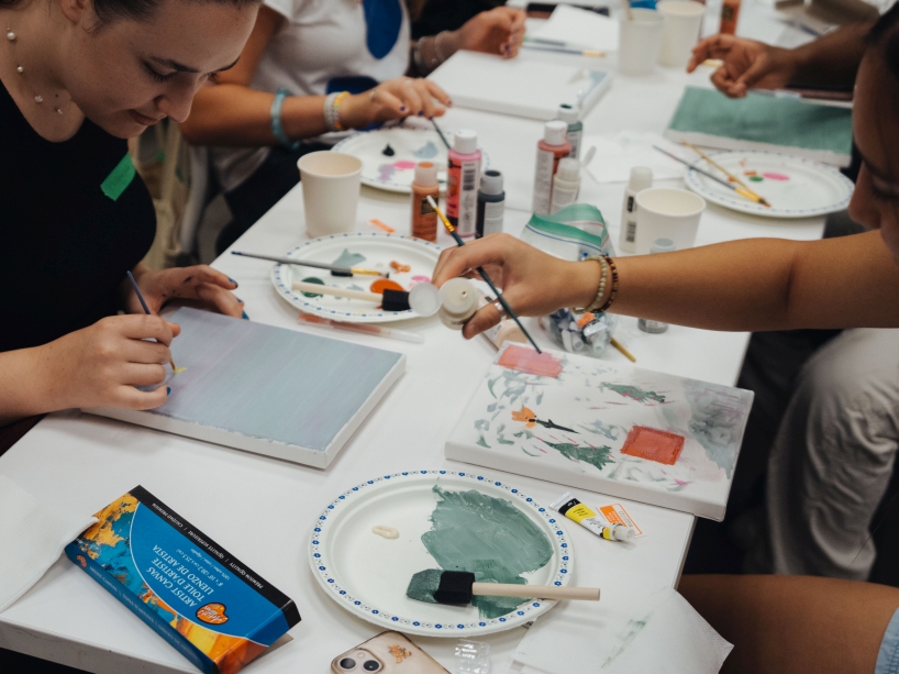 Students sit around a table and paint on small canvases.