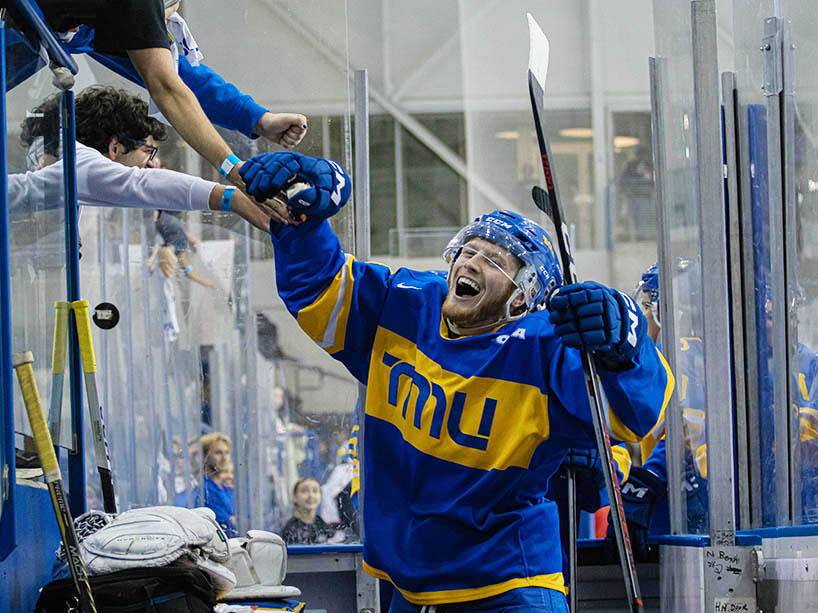 A hockey player smiles and high fives fans over the glass during a game.