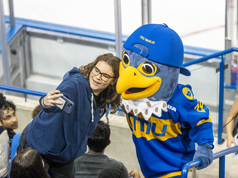 A student poses for a photo with a mascot.