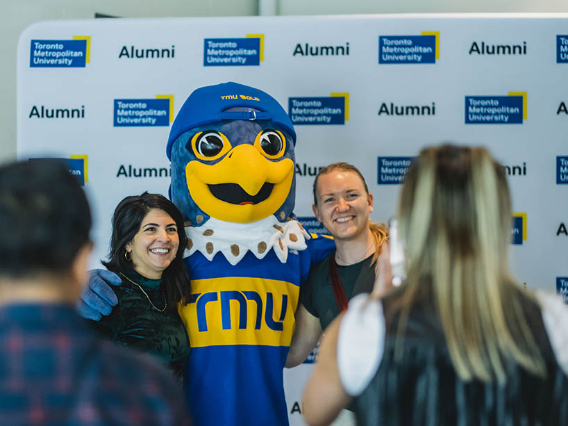 Two people pose for a photo with a mascot.