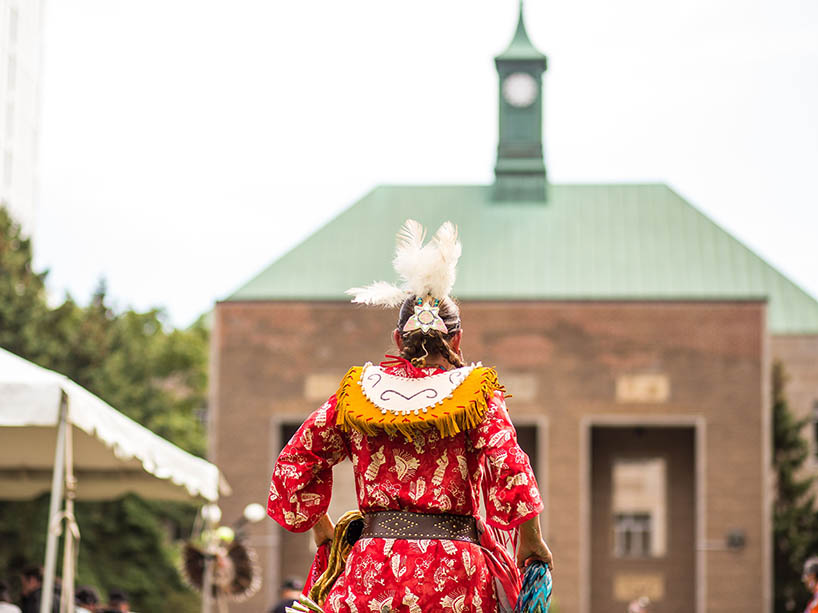 The back of a Pow Wow dancer, their regalia is bright and multi-coloured.