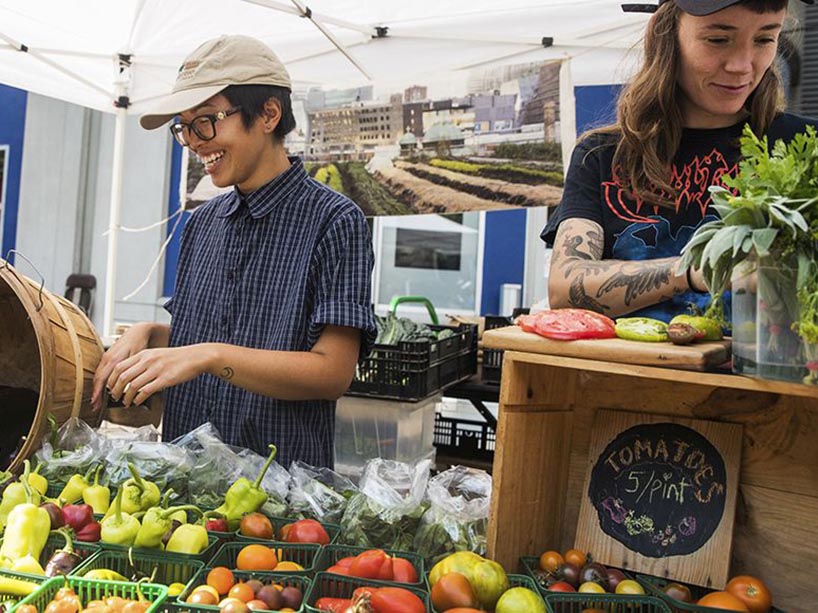 A vegetable and fruit stand with three workers standing behind the table.