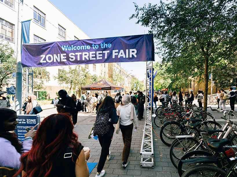 Students entering the street fair through an entrance with a banner that reads “Welcome to the Zone Street Fair”. 