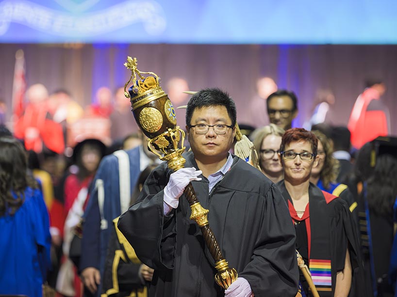 A man holds a ceremonial mace during a convocation ceremony.