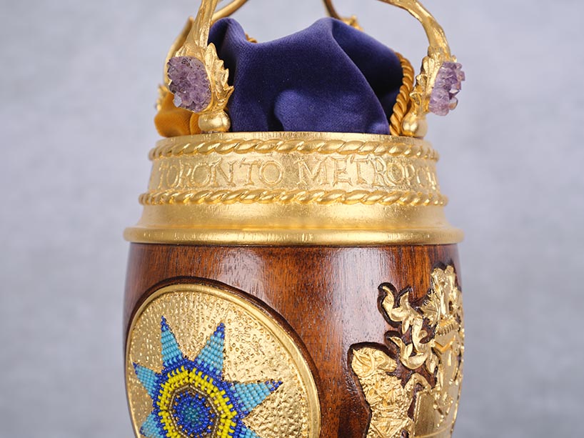 A close up photo of TMU’s mace shows the words “Toronto Metropolitan” carved into gold-painted wood.