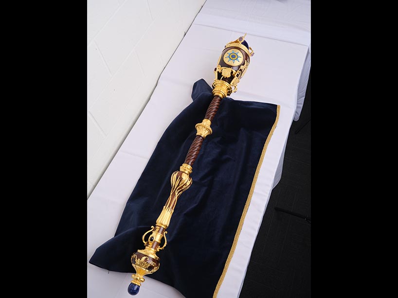 A wooded mace with painted gold detail, beadwork and gemstones.