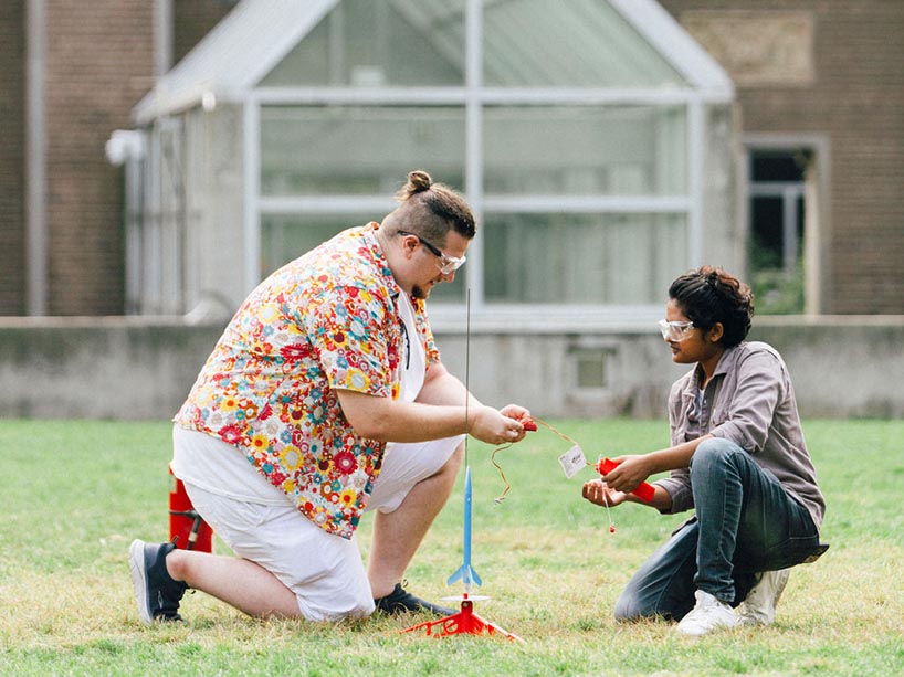 Two people set up a toy rocket launch in a field.