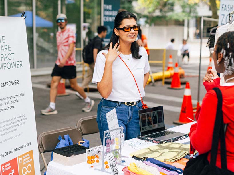 A woman stands at a display table talking to a student about her business.