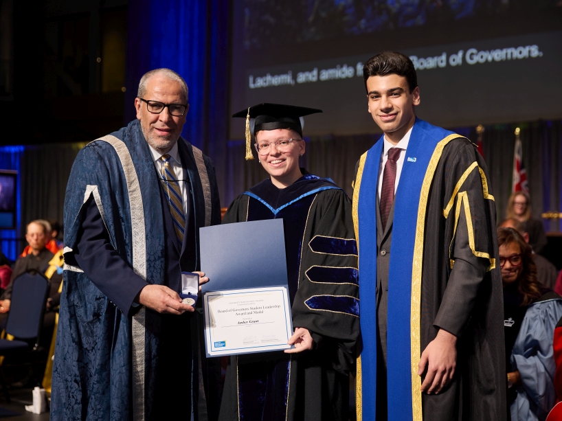 Three people wearing academic regalia pose for a photo while holding a certificate and a gold medal.