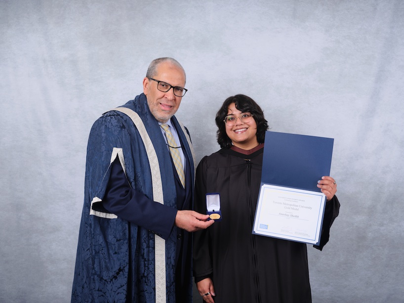 Two people wearing academic regalia pose for a photo while holding a certificate and a gold medal.