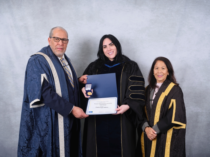 Three people wearing academic regalia pose for a photo while holding a certificate and a gold medal.