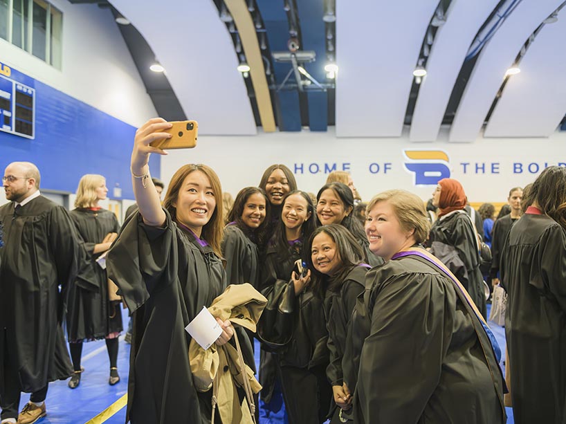 A group of women wearing academic regalia pose for a selfie.