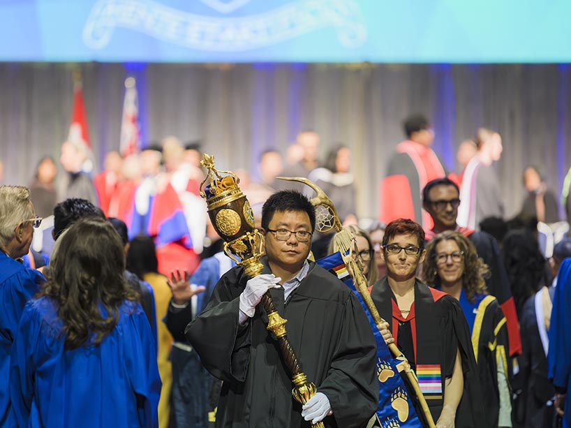 A man holds a decorative mace while leading a procession of people.