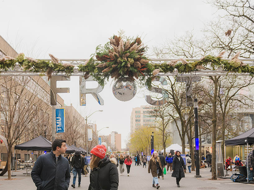 People walk under a large sign that says “Frost” on the Toronto Metropolitan University campus.