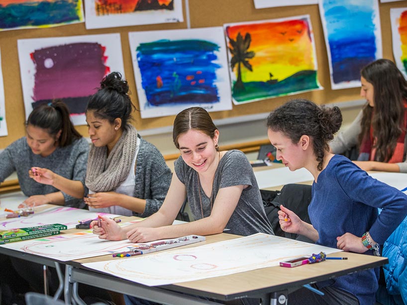 A group of students laughing together in an art class, surrounded by artworks on the walls.