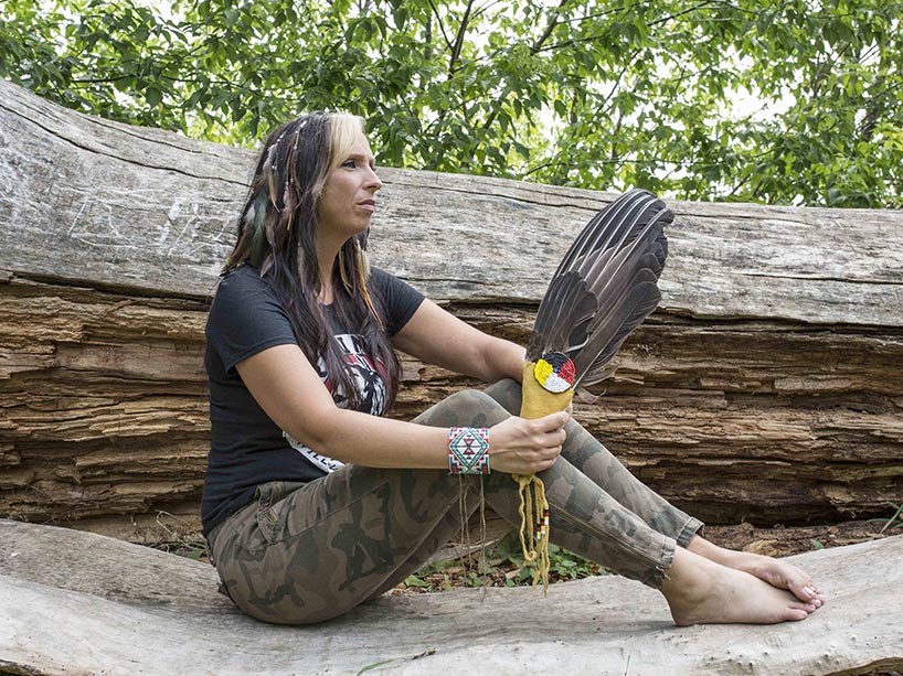 Pamela Palmater seated on a tree trunk, holding a feather in her hand.