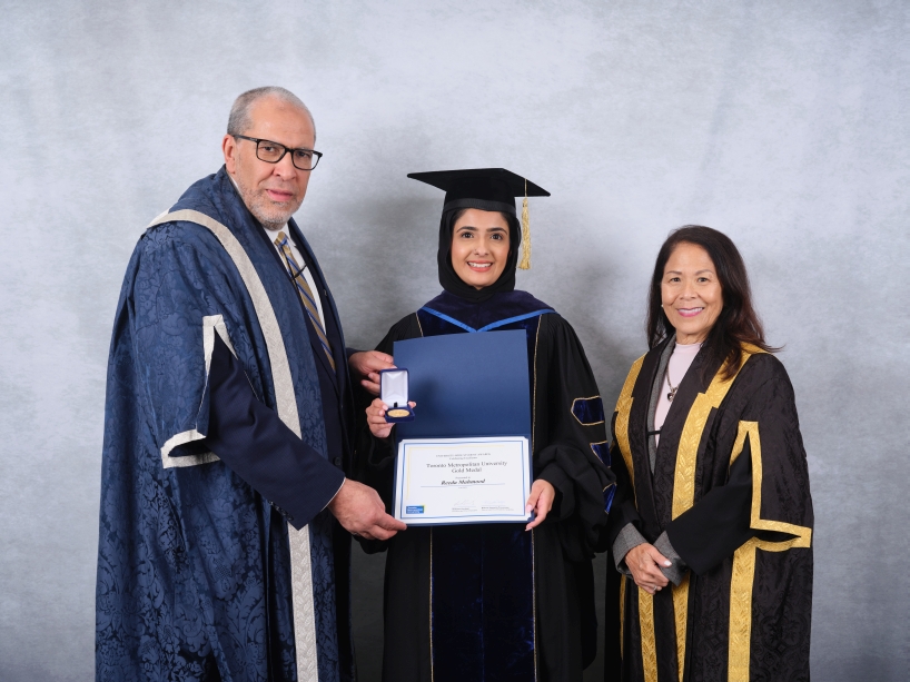 Three people wearing academic regalia pose for a photo while holding a certificate and a gold medal.