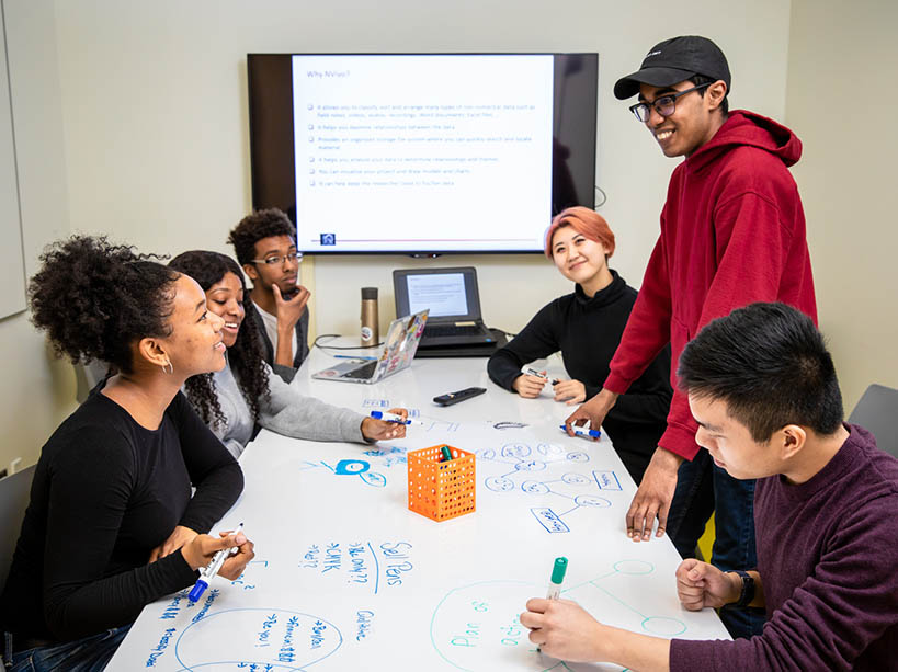 Six TMU students from different backgrounds in discussion around a table.