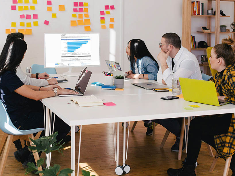 Five people sitting at a table looking at data on a big screen. 