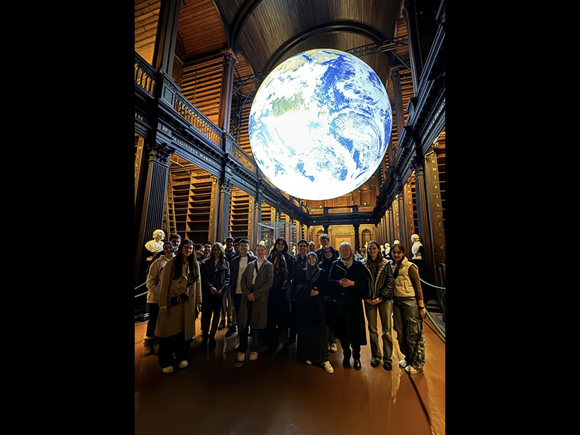 Winners of the Global Undergraduate awards standing in a wood paneled room, with a luminous globe hanging from the ceiling.