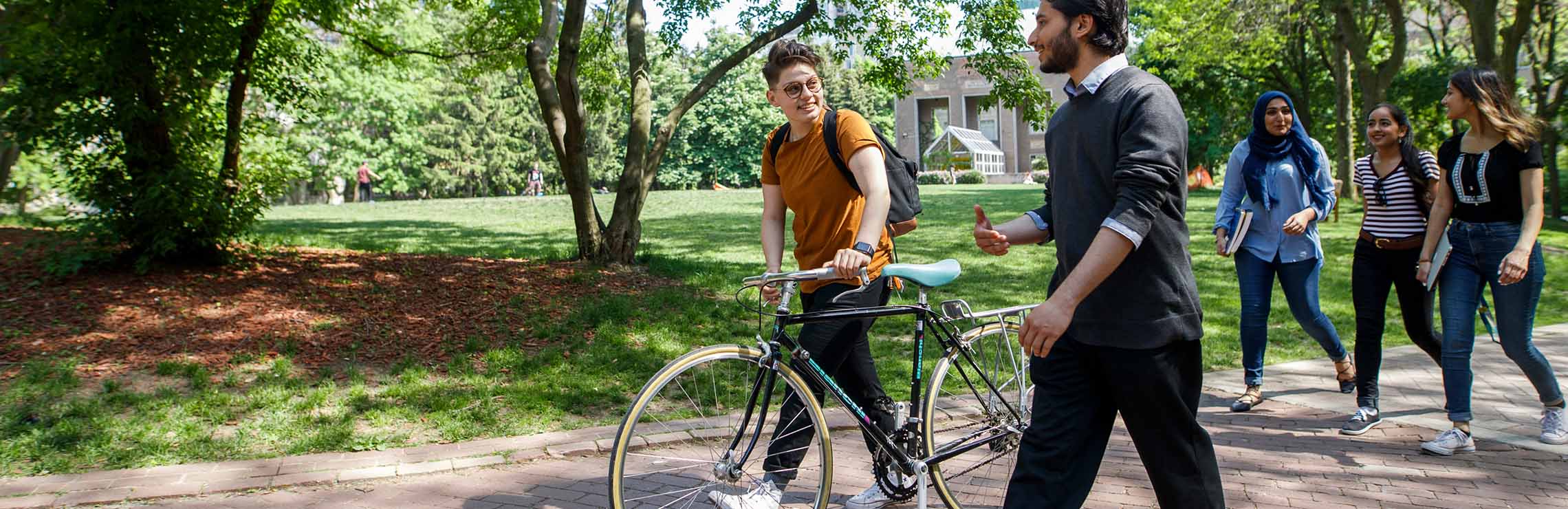 A group of students walking on campus, one person is walking their bike 