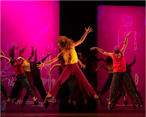 Dancers in front of bright fuscia backdrops jump with the limbs spread and look down to the side