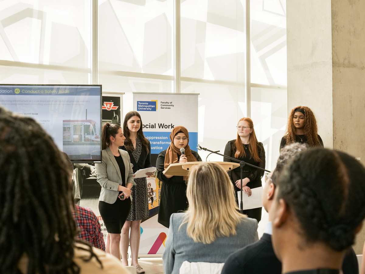 Five students at a podium in the SLC present in front of posters for Social Work and the TTC.