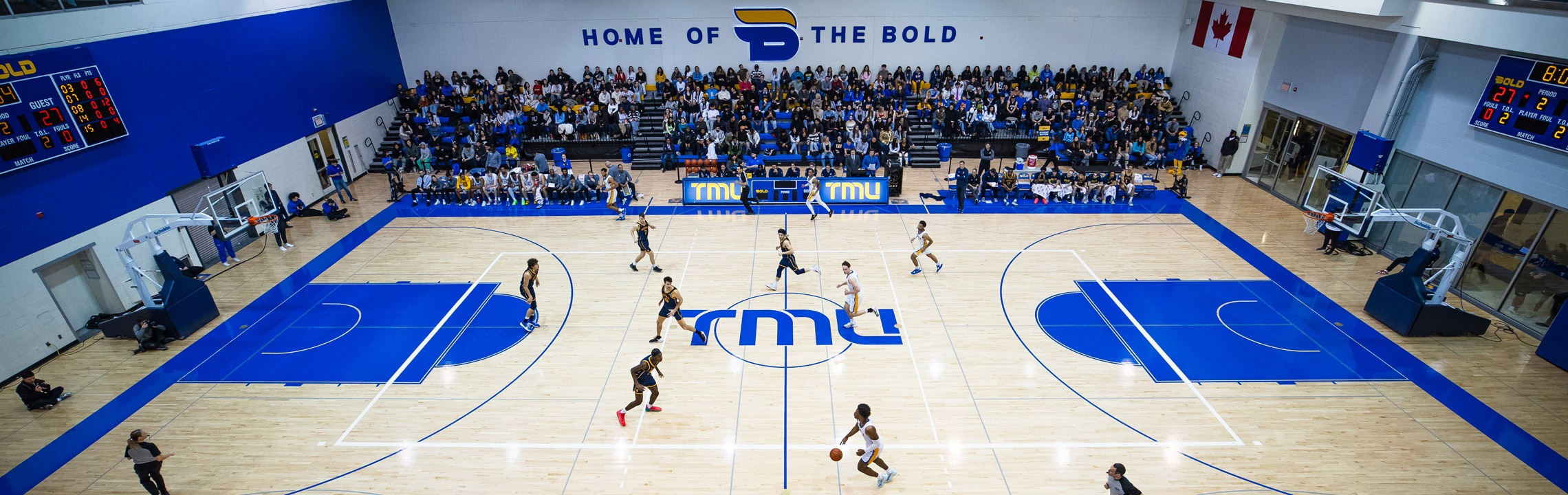 TMU Bold players dash across the Mattamy Athletic Centre Home Court during a basketball game.