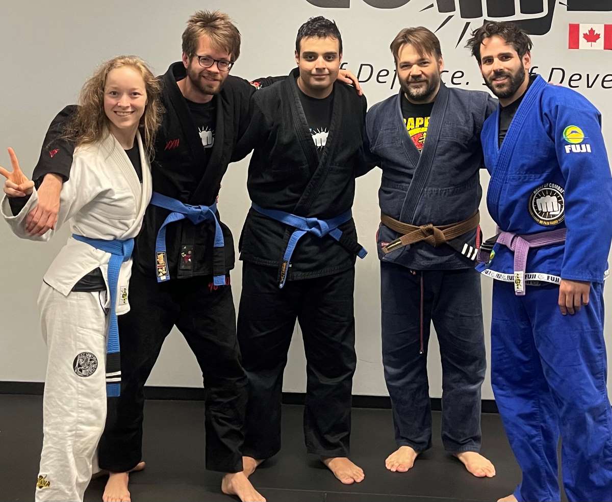 Two men practice Brazilian Jiu Jitsu on a blue mat surrounded by their class.