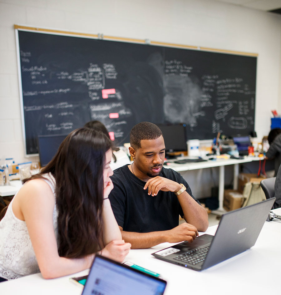 Two students are working together at the DFZ. They are working off one laptop.