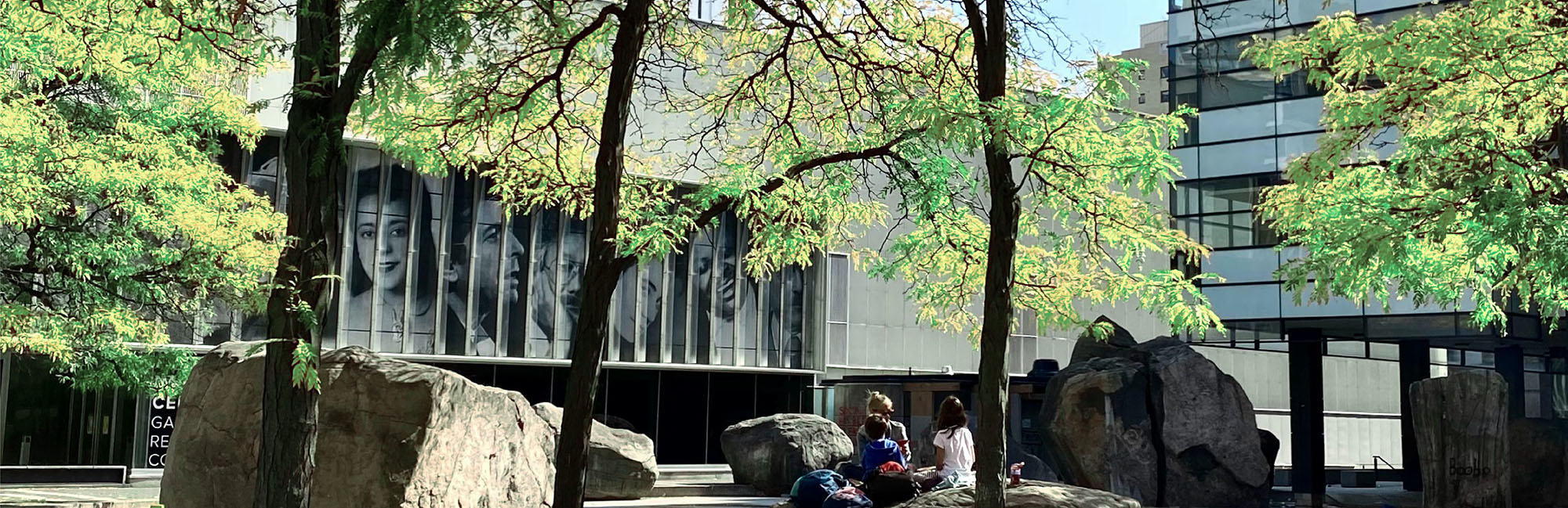 A family sits among the trees and rocks at Devonian Pond outside TMU's The Image Centre.