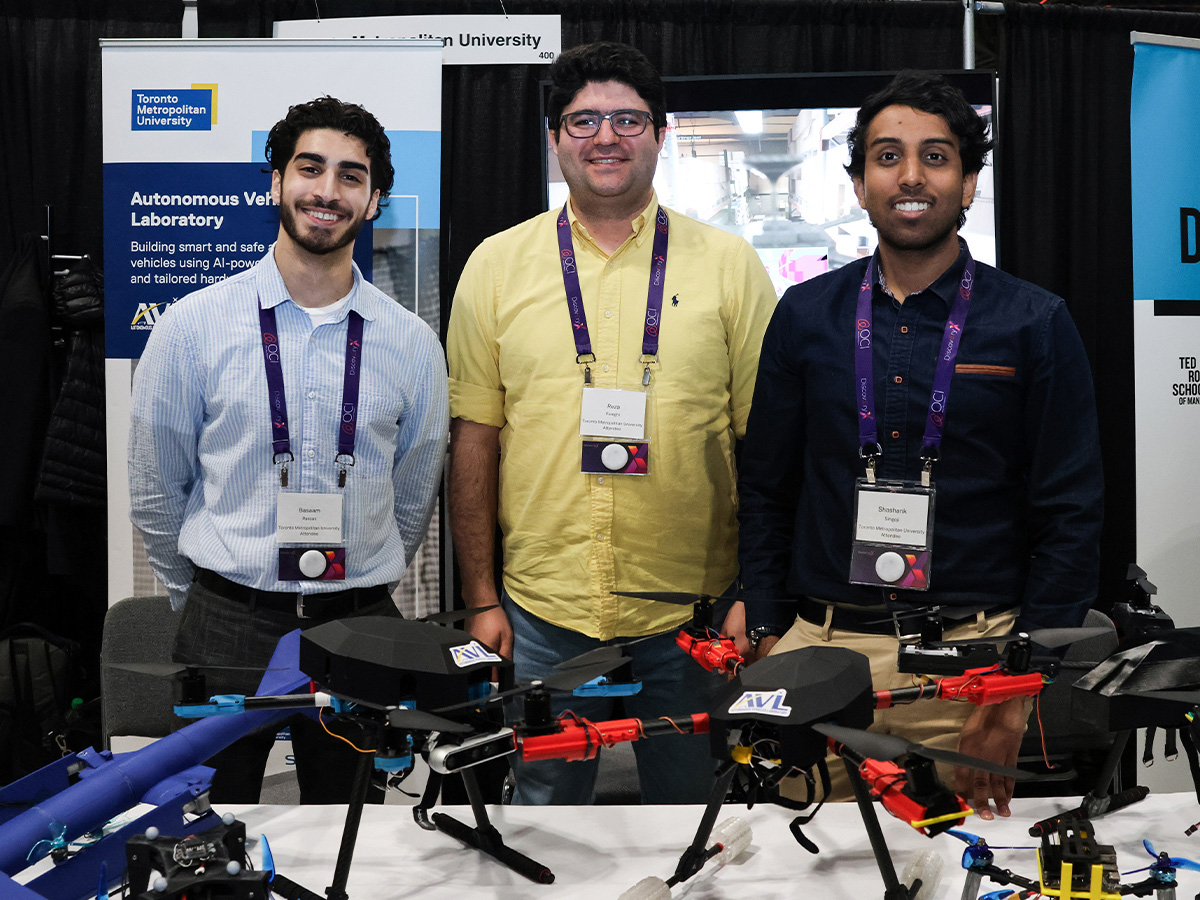 Professor Reza Faieghi and two students from his lab stand behind a table covered with drones. Photo credit: Zeeanna Ibrahim/Zone Learning at Toronto Metropolitan University