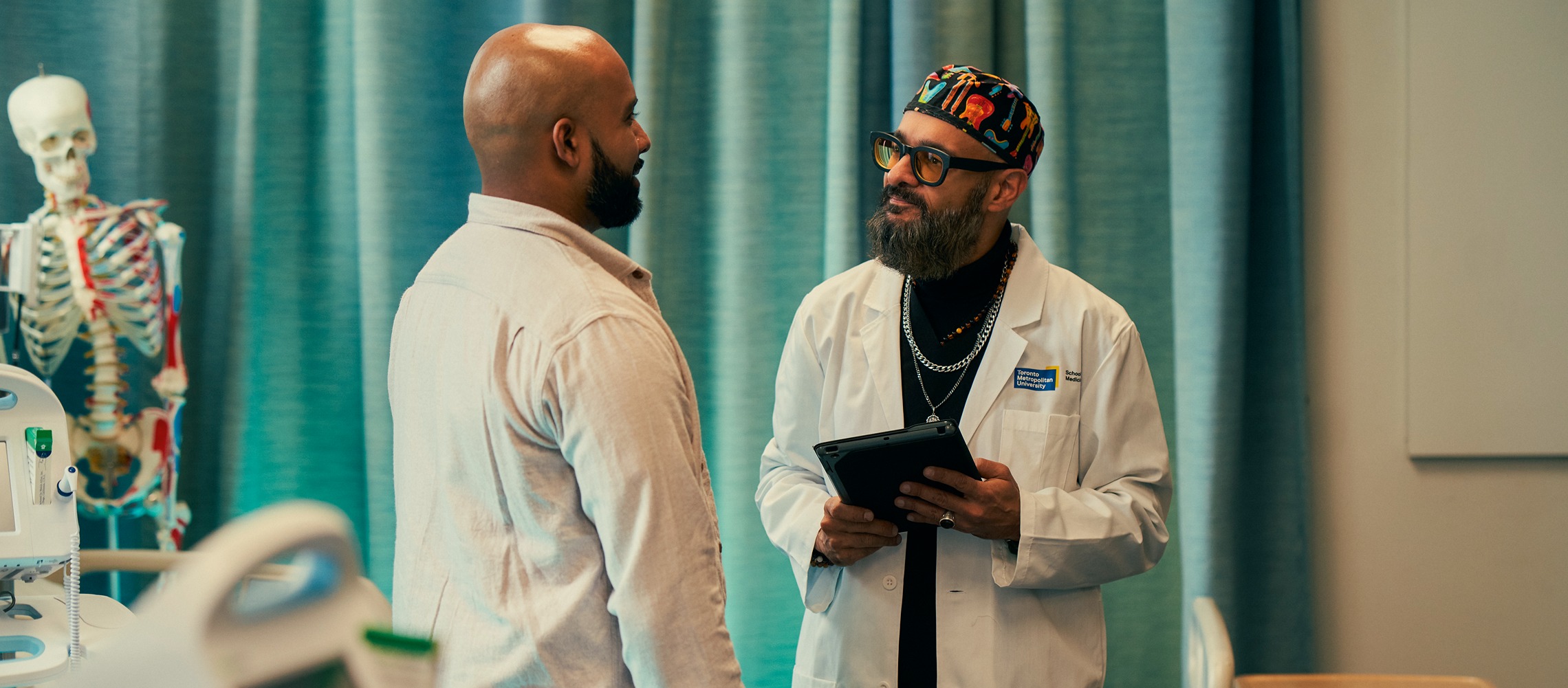 A South Asian male doctor consults with an adult male patient in a hospital room