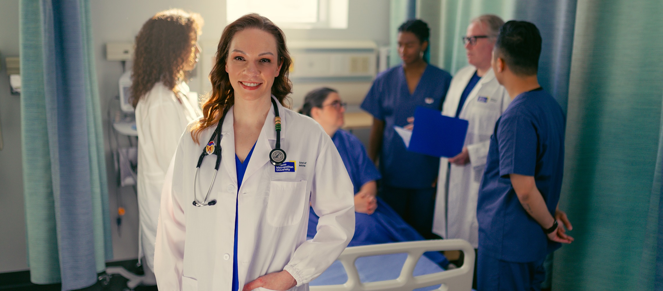 An Indigenous female doctor stands in a busy hospital ward