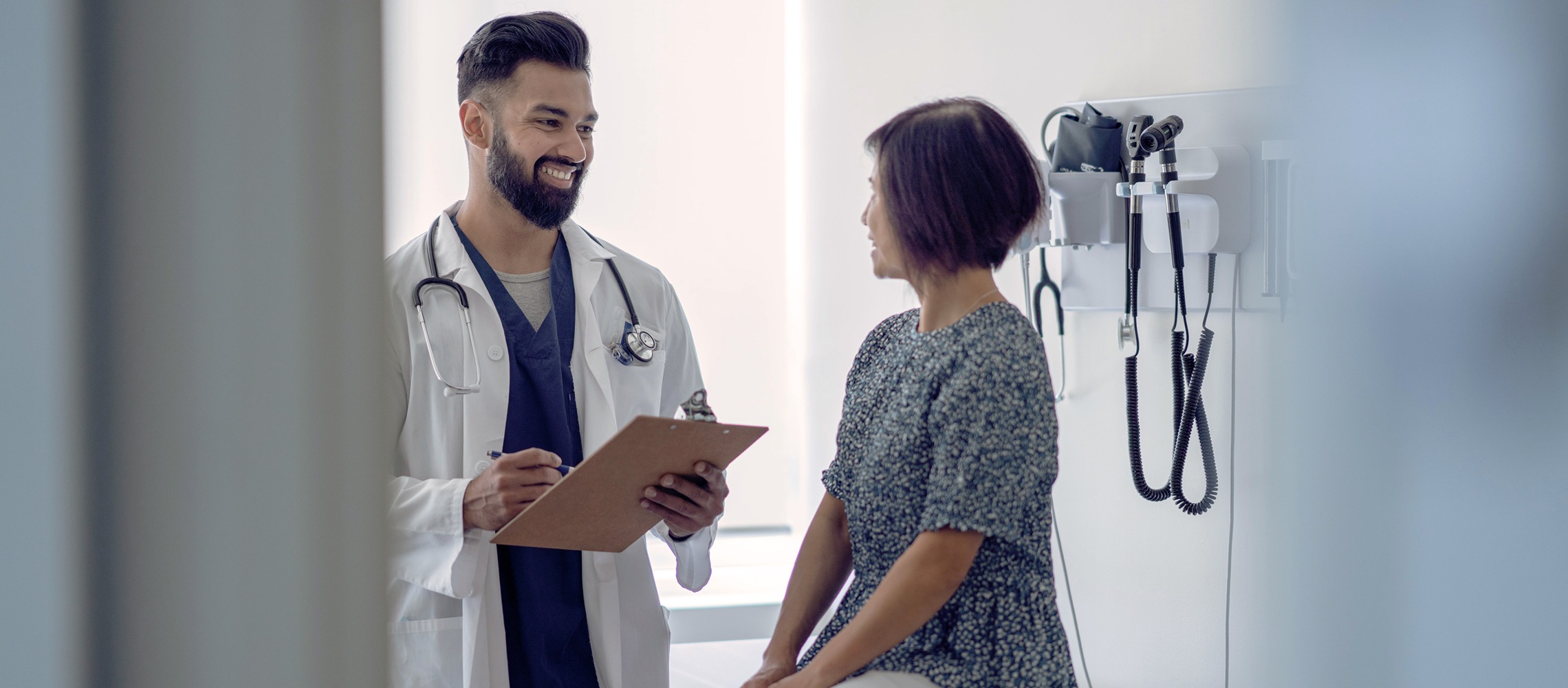 A male doctor speaks with a female patient in an exam room