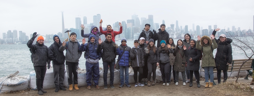 Group of students stand by Lake Ontario with the foggy Toronto skyline behind them