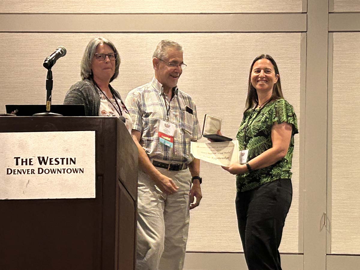 Professor Janet Koprivnikar receiving Henry Baldwin Ward Medal beside two presenters.