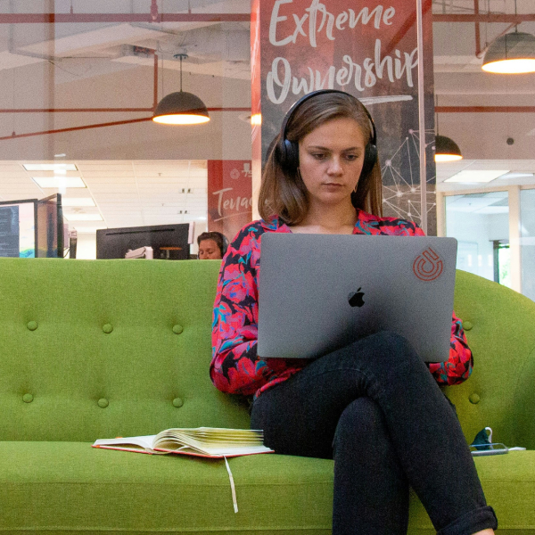 Woman sitting in office working on her laptop wearing headphones.