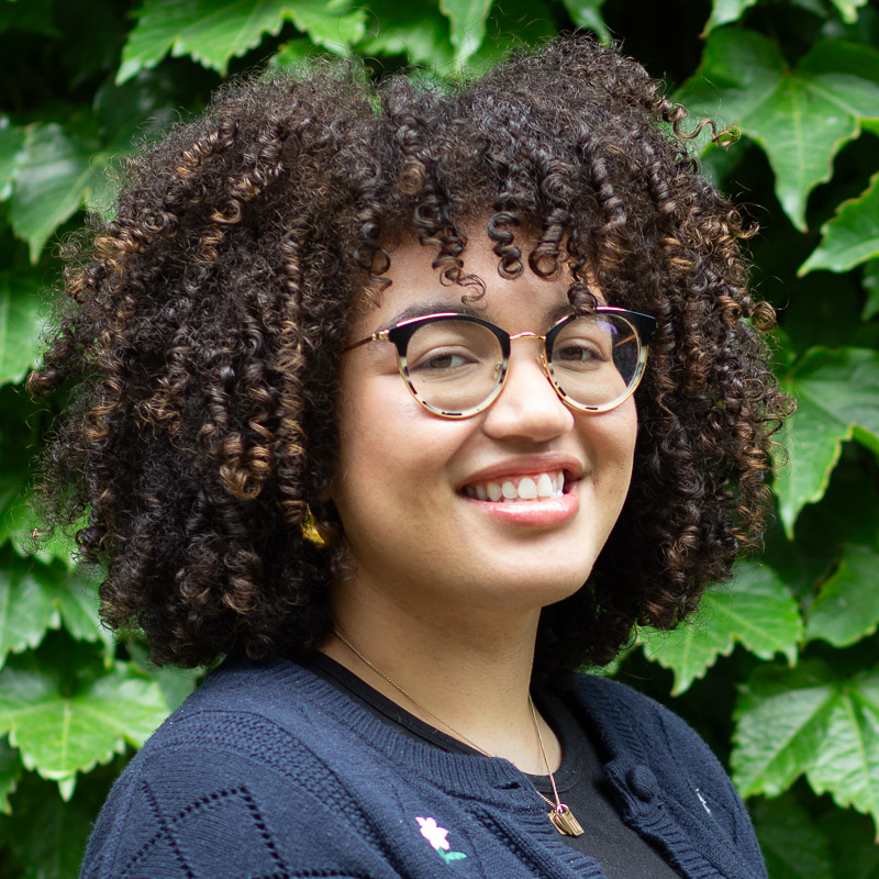 headshot of Eliza, smiling, curly brown hair, glasses