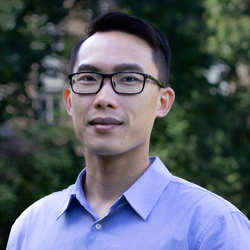 headshot of Huy Nguyen smiling slightly, wearing dark rimmed glasses and blue button-down shirt