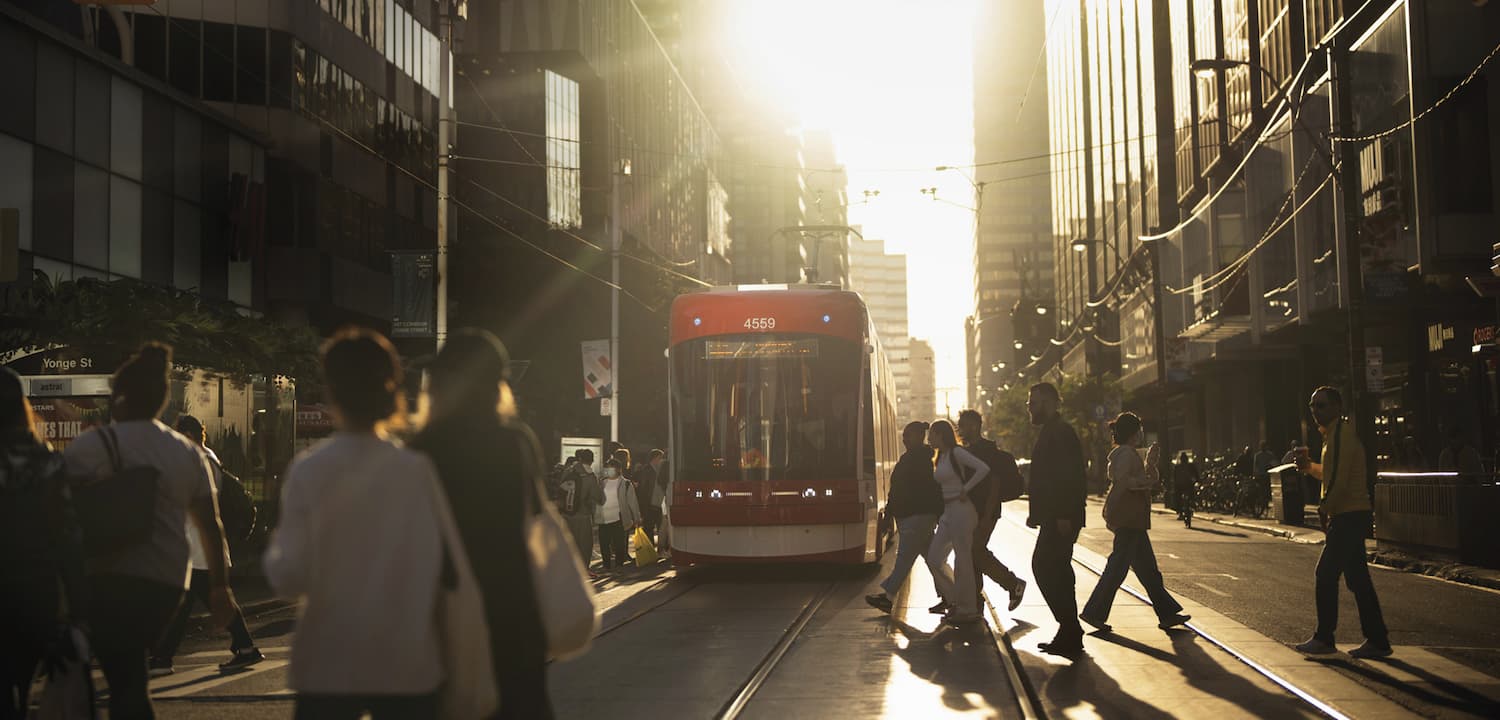 A red and white Toronto streetcar on a busy downtown street, framed by tall glass buildings and surrounded by pedestrians.