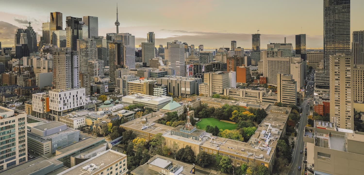 Aerial view of a cityscape with tall skyscrapers, a prominent tower, and a large green park surrounded by smaller buildings in the foreground.