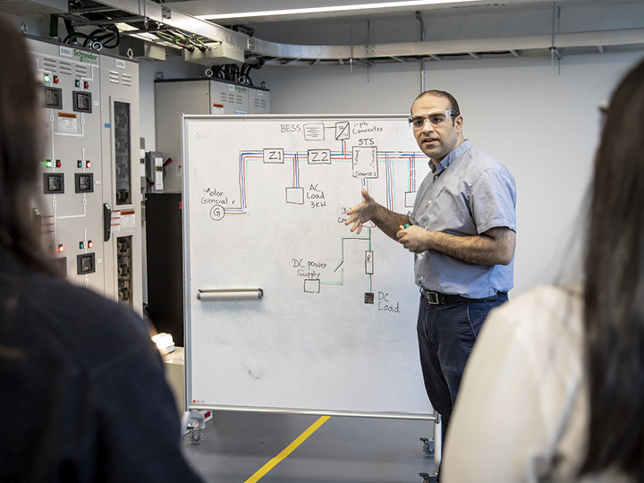 An instructor explains a system diagram on a whiteboard to students.