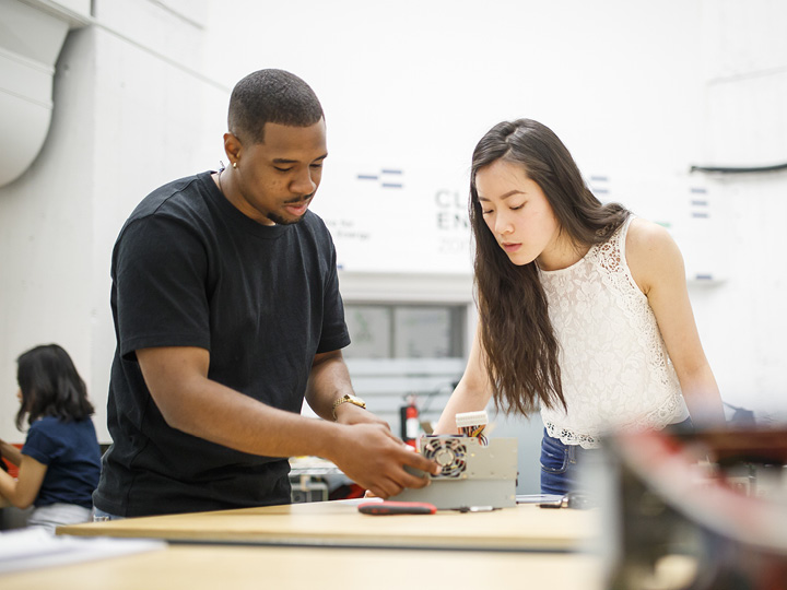 Two students examine an electrical component together in a lab setting.