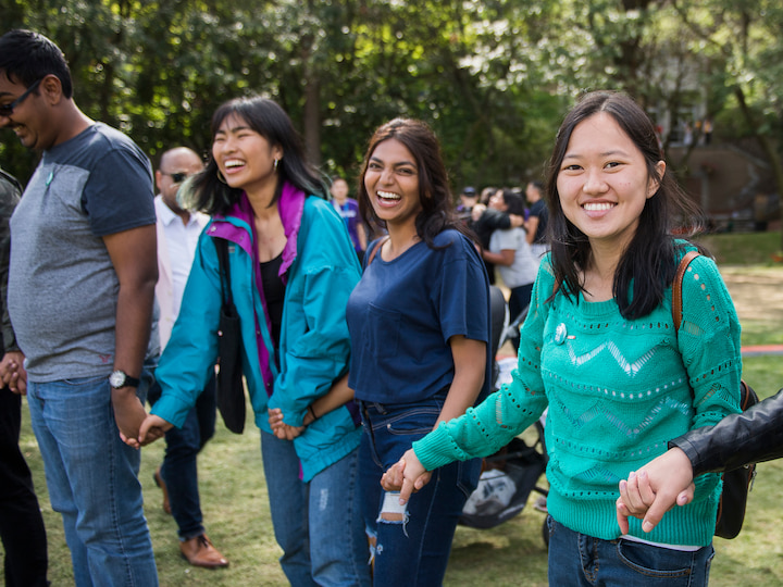 Students standing outside, smiling and holding hands.