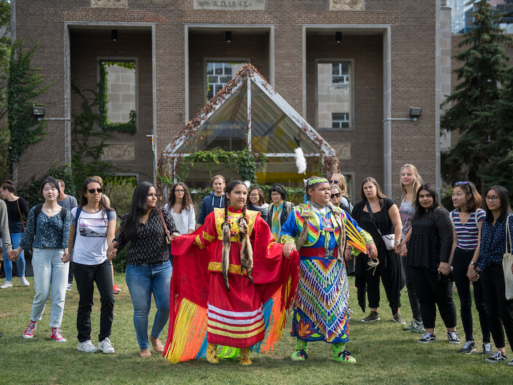 An Indigenous person in traditional outfit participating in a celebration, surrounded by spectators and community members