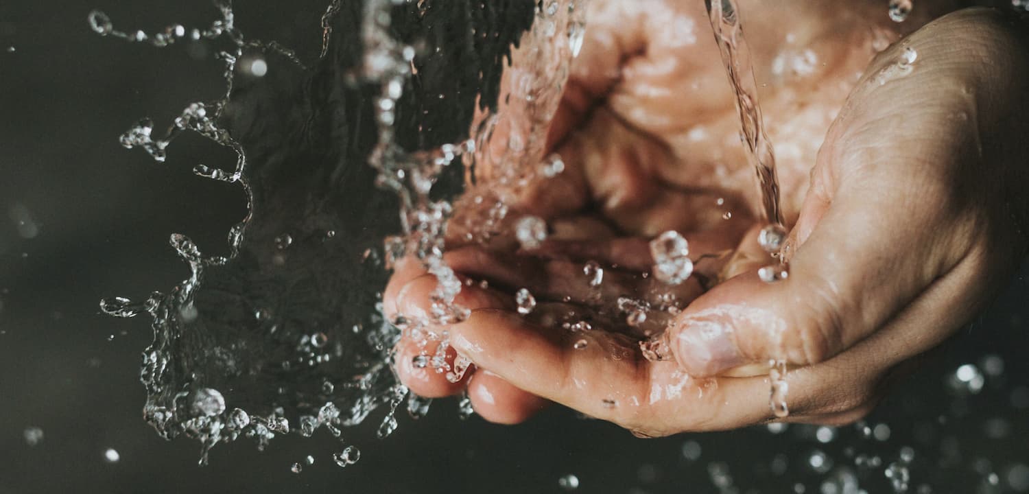 Close-up of hands cupped together, catching splashing water droplets.