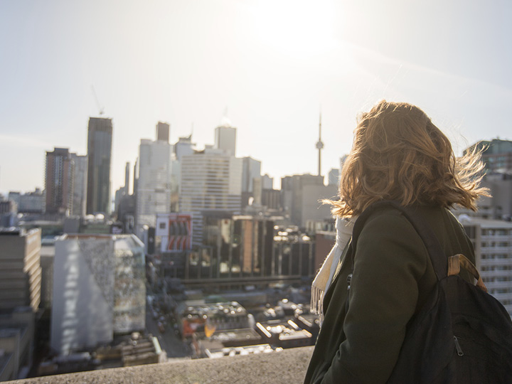 Person with a backpack looking out over a city skyline in bright daylight.